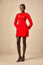 A woman wearing a red mini dress with long sleeves and a large bow detail at the neckline