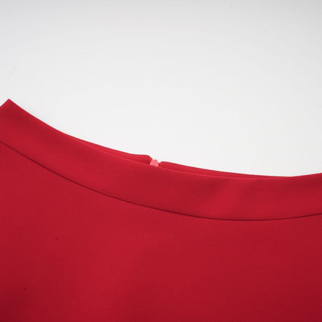 A woman wearing a red pleated blouse paired with a matching red pleated skirt standing against a plain background