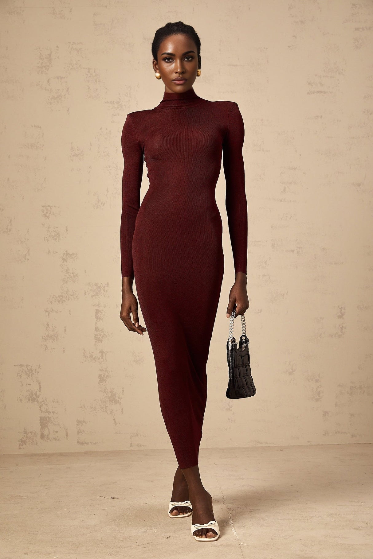 A woman wearing a red semisheer knitted midi dress with long sleeves standing against a plain background