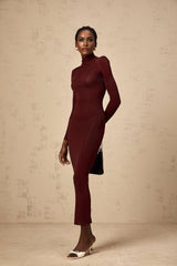 A woman wearing a red semisheer knitted midi dress with long sleeves standing against a plain background