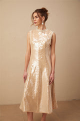 A woman wearing a shimmering midi dress adorned with faux pearls and sequins posing elegantly against a plain background