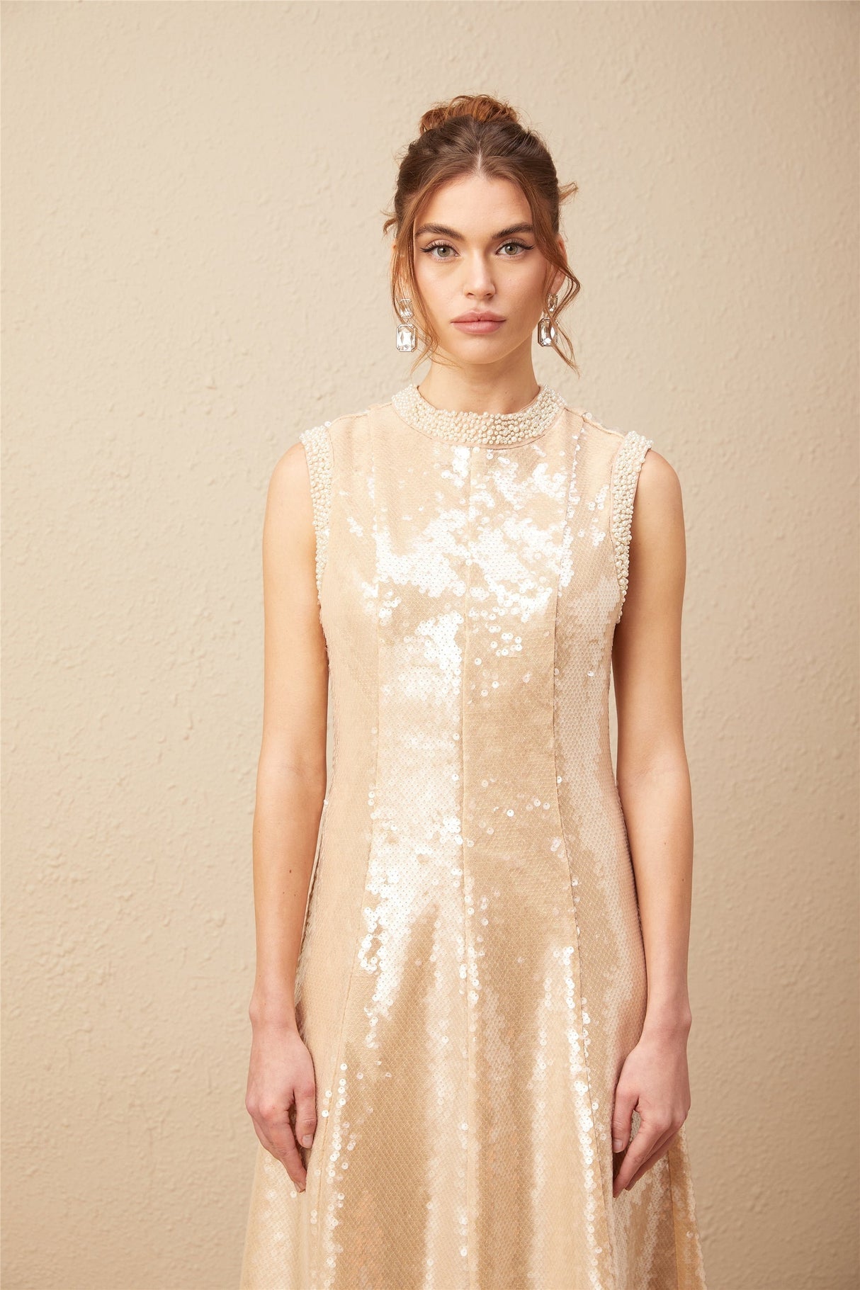 A woman wearing a shimmering midi dress adorned with faux pearls and sequins posing elegantly against a plain background