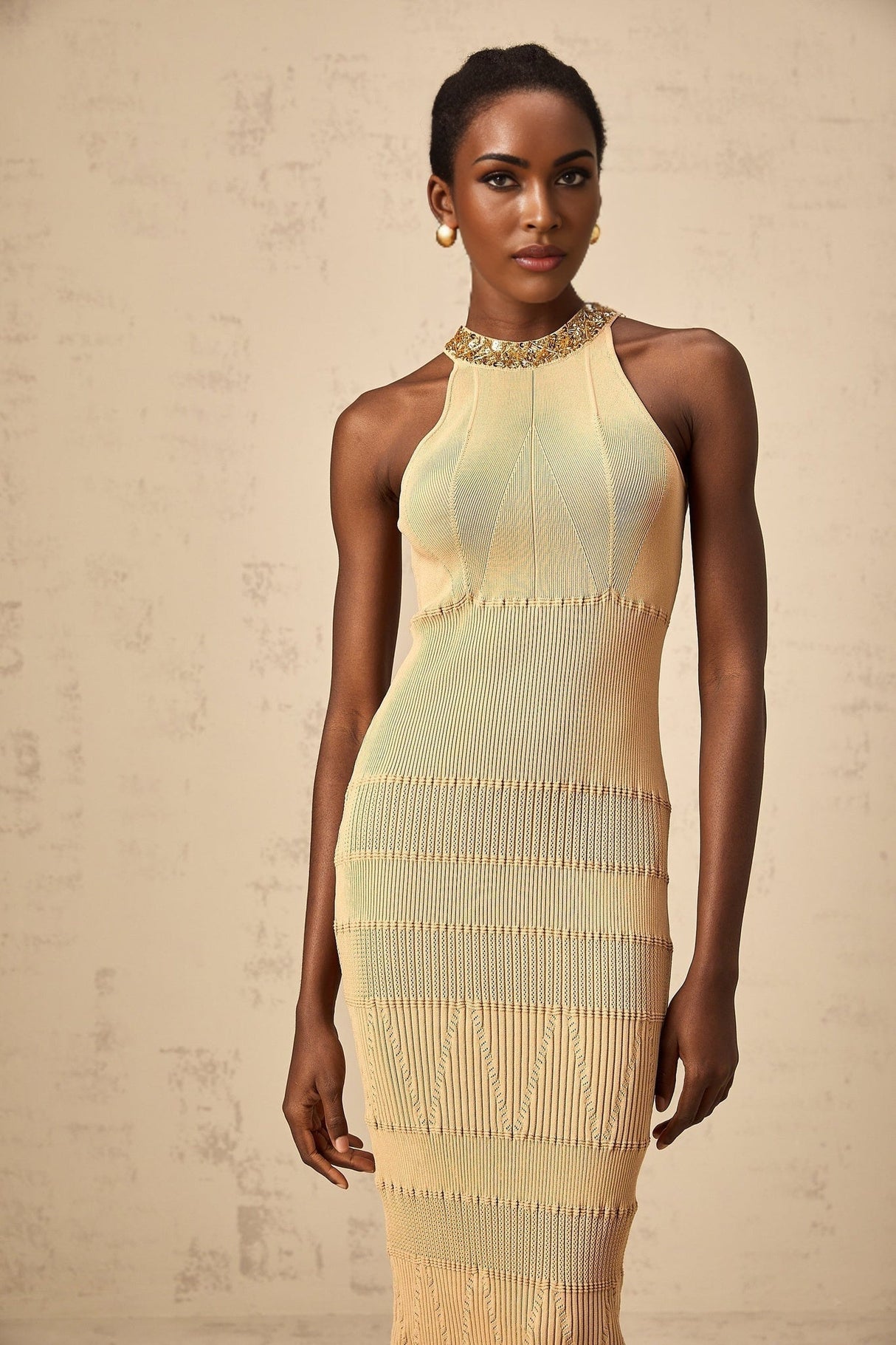 A woman wearing a shimmering sequined midi dress with ribbed texture in a fitted silhouette standing against a plain background