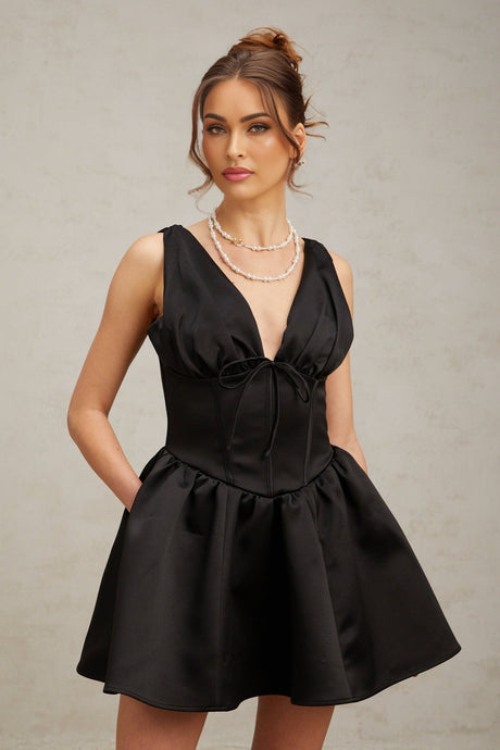 A woman wearing a short black dress with a Vneckline and flared skirt standing against a plain background