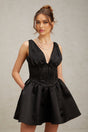 A woman wearing a short black dress with a Vneckline and flared skirt standing against a plain background