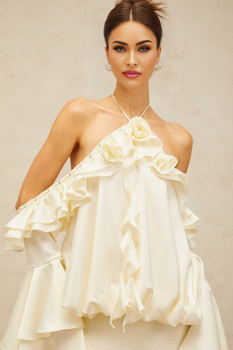 A woman wearing a short floral dress with ruffled sleeves and exposed shoulders standing against a plain background