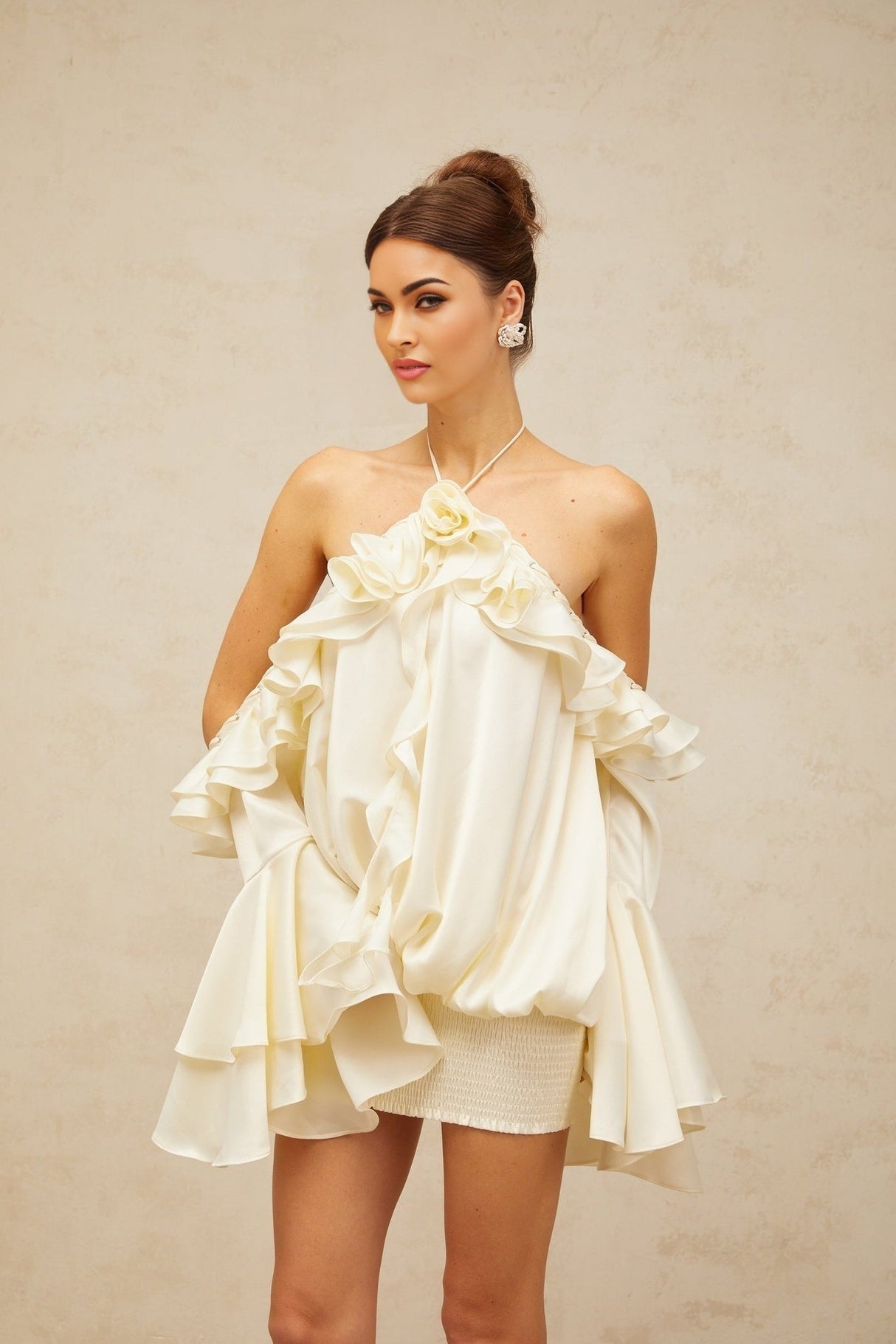 A woman wearing a short floral print dress with ruffled details and exposed shoulders standing against a plain background