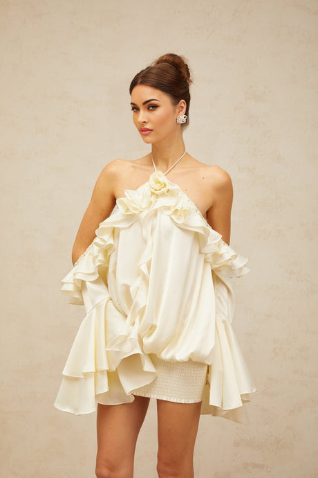 A woman wearing a short floral print dress with ruffled details and exposed shoulders standing against a plain background