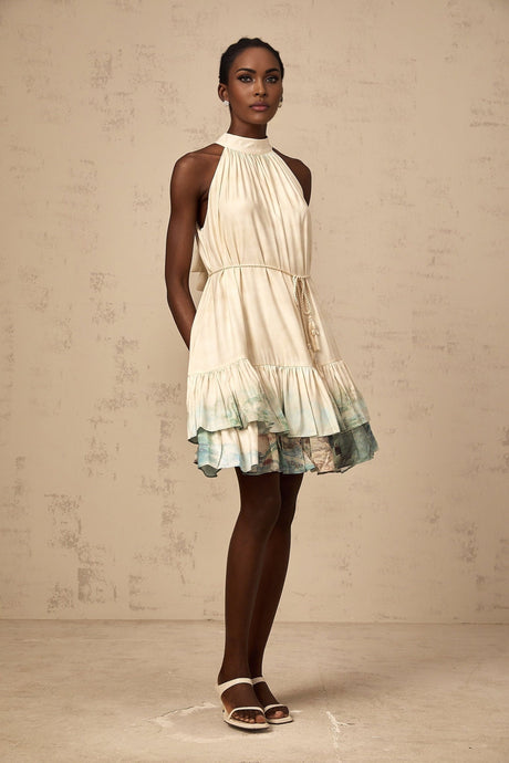 A woman wearing a short multicolored layered dress with a mixed pattern print standing against a plain background