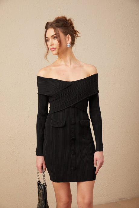 A woman wearing a short offshoulder dress in a ribbed knit fabric The dress is form fitting and has a mini length with long sleeves The model is shown standing in a casual pose
