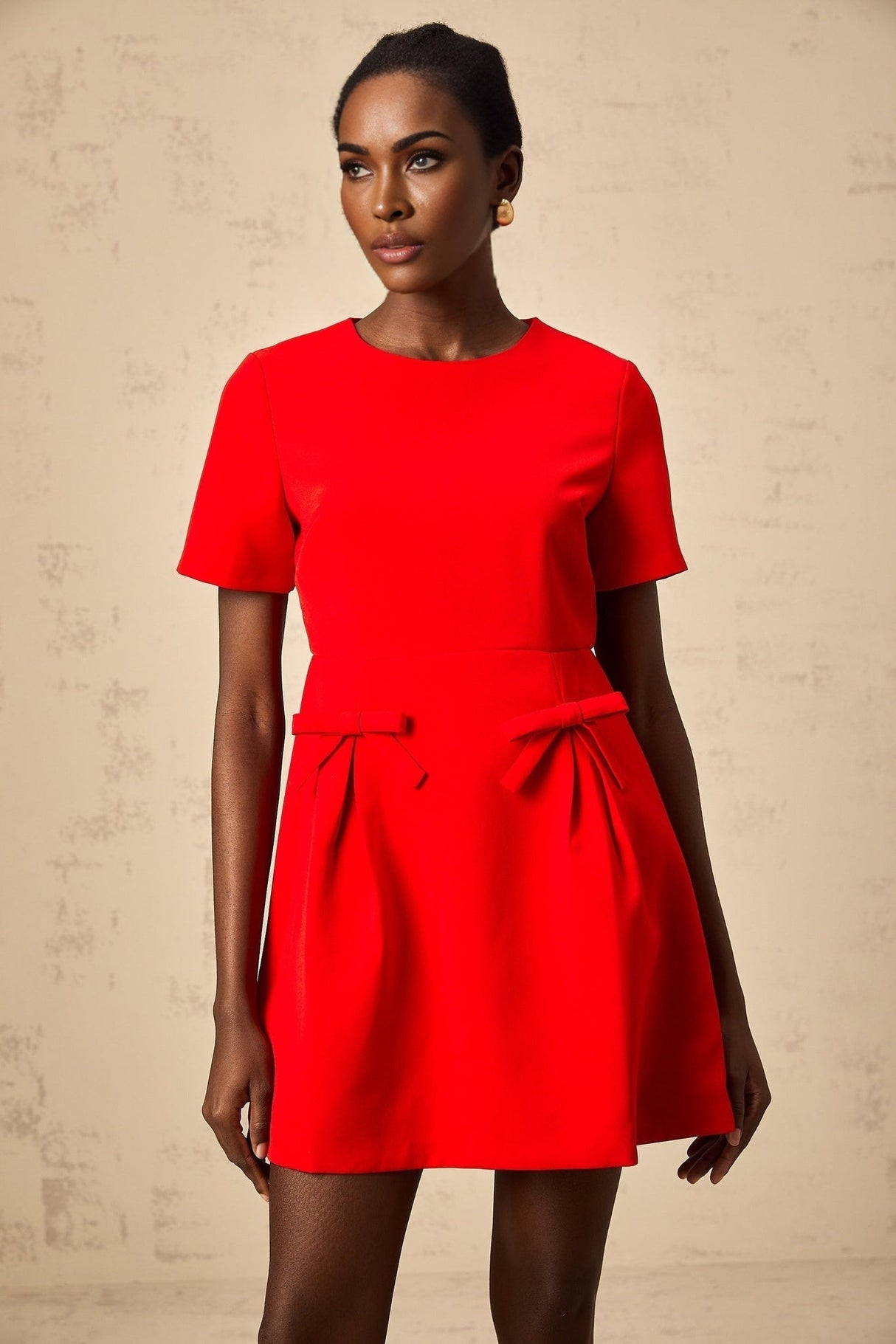 A woman wearing a short red mini dress with short sleeves and a decorative bow detail