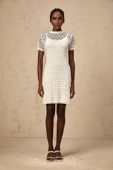 A woman wearing a short white semisheer knit dress standing in a neutral background