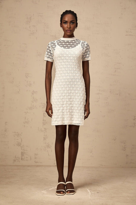 A woman wearing a short white semisheer knit dress standing in a neutral background