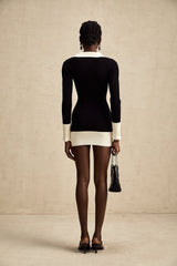 A woman wearing a short wool dress with color block design and ribbed knit texture standing against a plain background