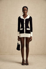 A woman wearing a short wool dress with color blocks and ribbed knit texture featuring long sleeves and a high neckline
