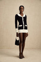 A woman wearing a short wool dress with colorblocked panels and ribbed knit texture featuring contrasting shades and a slim fit silhouette
