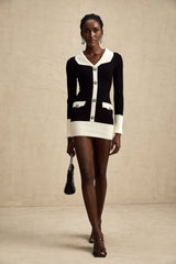 A woman wearing a short wool dress with colorblocked panels and ribbed knit texture The dress features contrasting colors and a fitted silhouette