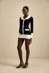 A woman wearing a short wool dress with colorblocked sections and ribbed knit texture The dress features contrasting colors and a fitted silhouette