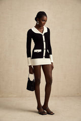A woman wearing a short wool dress with colorblocked sections and ribbed knit texture The dress features contrasting colors in a geometric pattern and has a fitted silhouette with long sleeves