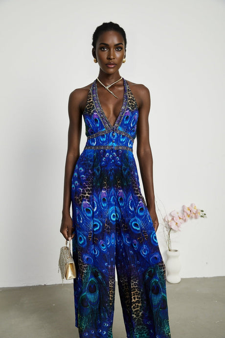 A woman wearing a sleek silk jumpsuit with a halter neckline in a soft flowing fabric the garment drapes elegantly and features a fitted waist with wide leg pants