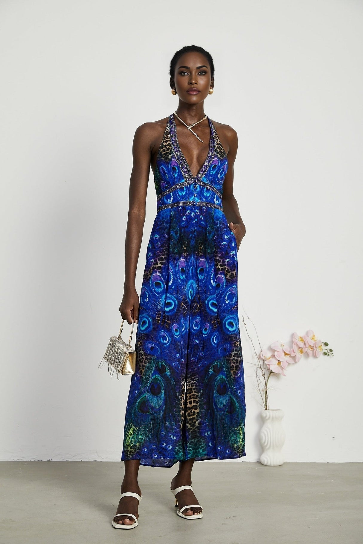 A woman wearing a sleek silk jumpsuit with a halter neckline in a stylish silhouette standing in a relaxed pose against a plain background