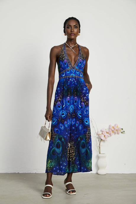 A woman wearing a sleek silk jumpsuit with a halter neckline in a stylish silhouette standing in a relaxed pose against a plain background