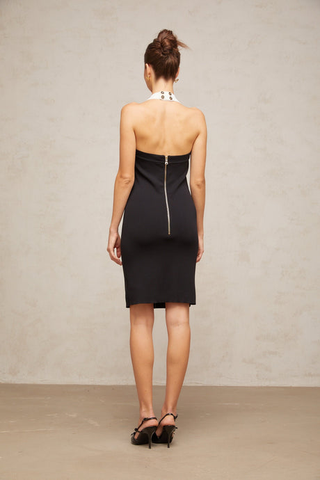A woman wearing a sleeveless halterneck knit mini dress with colorblocked design featuring contrasting colors on the top and bottom portions of the dress