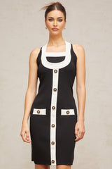 A woman wearing a sleeveless halterneck knit mini dress with colorblocked design featuring contrasting sections in different colors The dress has a form fitting silhouette and ends above the knee