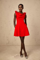 A woman wearing a sleeveless red mini dress with faux flower details standing against a plain background