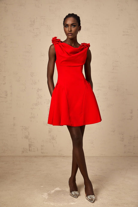 A woman wearing a sleeveless red mini dress with faux flower details standing against a plain background