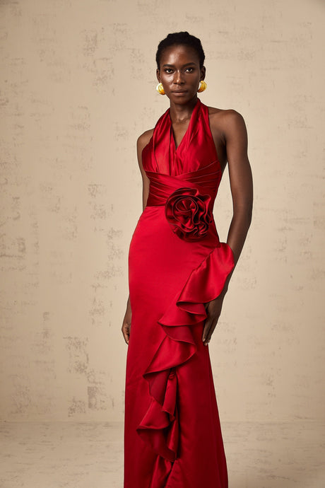 A woman wearing a vibrant red halterneck maxi dress with 3D petal ruffles cascading down the length of the gown creating a dramatic and elegant silhouette