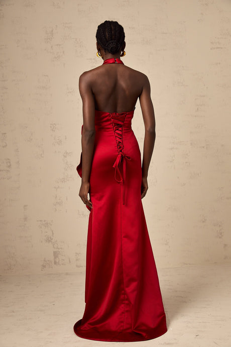 A woman wearing a vibrant red halterneck maxi dress with ruffled 3D petal details cascading down the length of the gown creating a dramatic and elegant silhouette