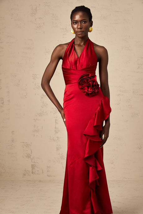 A woman wearing a vibrant red halterneck maxi dress with ruffled 3D petal details cascading down the length of the gown