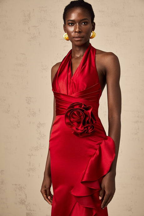 A woman wearing a vibrant red halterneck maxi dress with ruffled 3D petal details cascading down the length of the gown