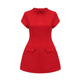 A woman wearing a vibrant red mini dress with cap sleeves standing against a plain background