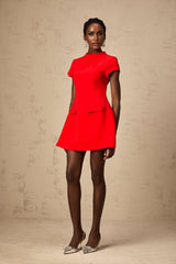 A woman wearing a vibrant red mini dress with cap sleeves standing against a plain background