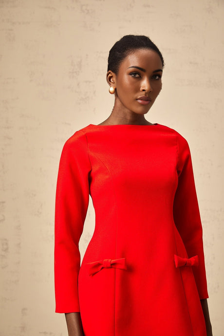 A woman wearing a vibrant red mini dress with long sleeves and a large bow detail at the waist