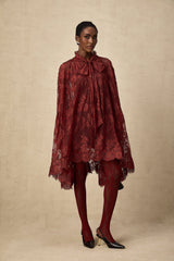 A woman wearing a vibrant red oversize dress made of delicate chantilly lace standing in a relaxed pose against a plain background