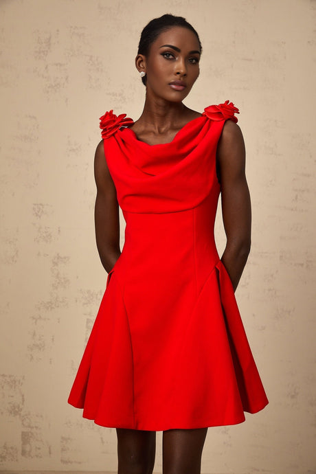A woman wearing a vibrant red sleeveless mini dress with faux flower details standing against a plain background