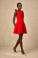 A woman wearing a vibrant red sleeveless mini dress with faux flower embellishments standing in a neutral background