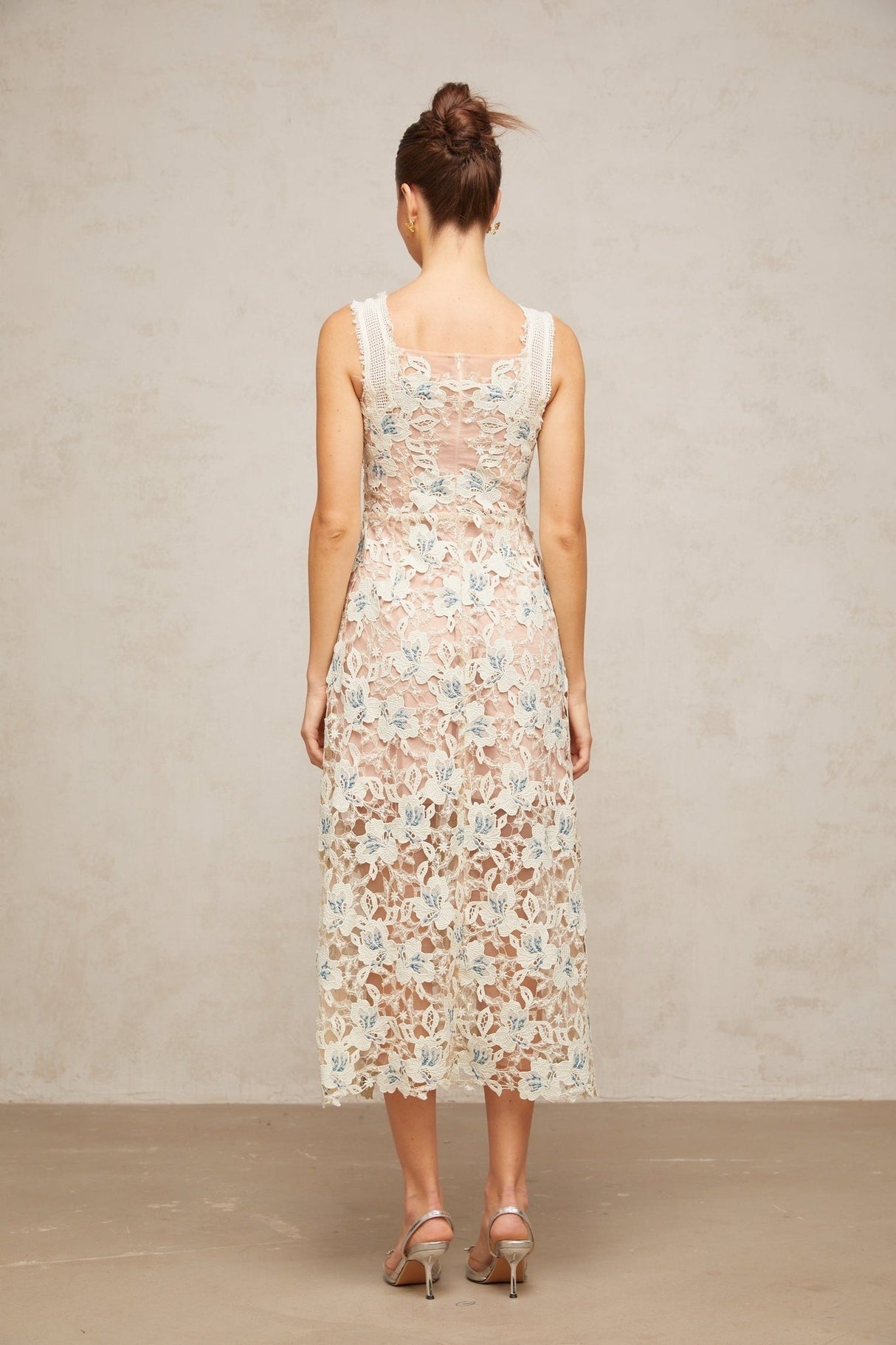 A woman wearing a white Aline midi dress with floral lace detailing standing against a plain background