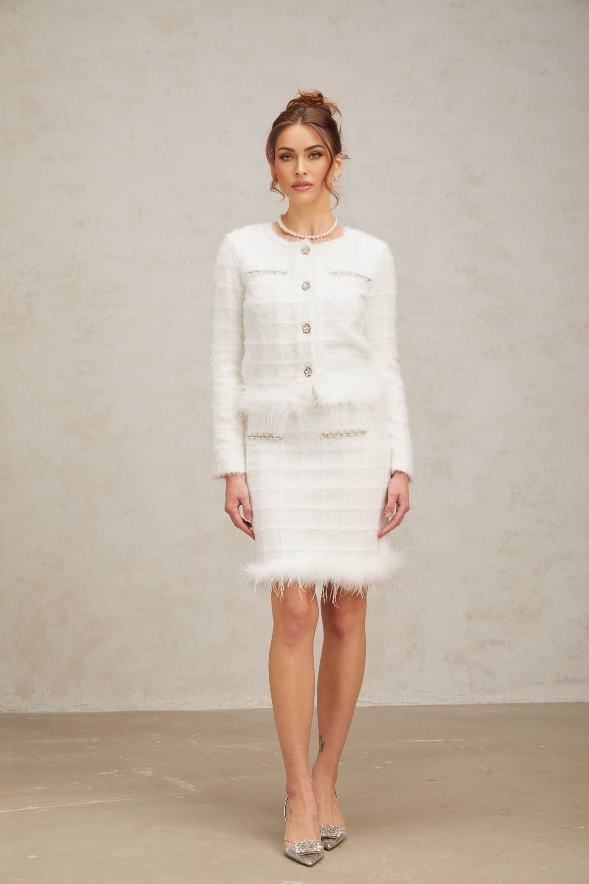 A woman wearing a white feather textured waffle knit cardigan and matching skirt set standing against a plain background