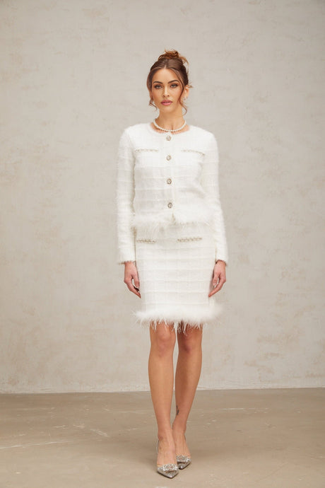A woman wearing a white feather textured waffle knit cardigan and matching skirt set standing against a plain background