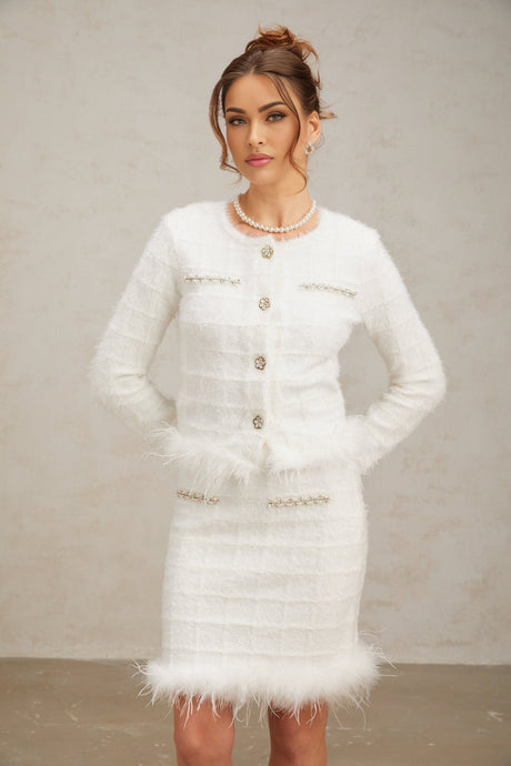 A woman wearing a white feather waffle knit cardigan and matching skirt set standing against a plain background