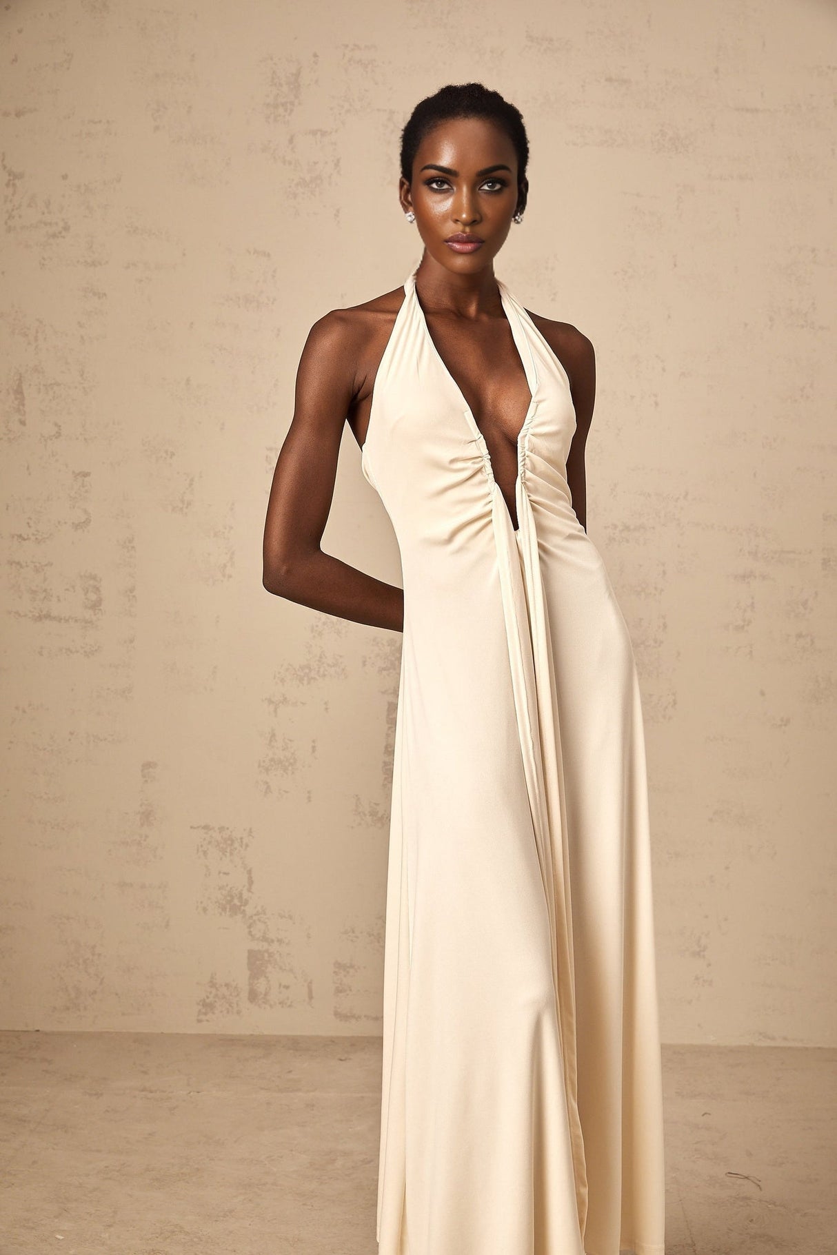 A woman wearing a white floorlength maxi dress with a deep V neckline and draped fabric detail