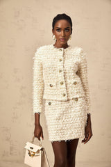 A woman wearing a white fluffy knit cardigan paired with a matching skirt set against a plain background