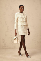 A woman wearing a white fuzzy knit cardigan and matching skirt set standing against a plain background