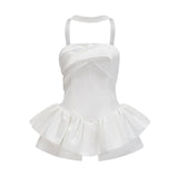 A woman wearing a white halterneck mini dress with ruffled details standing against a plain background