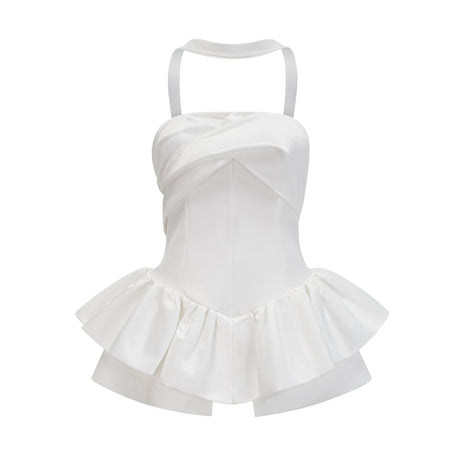 A woman wearing a white halterneck mini dress with ruffled details standing against a plain background