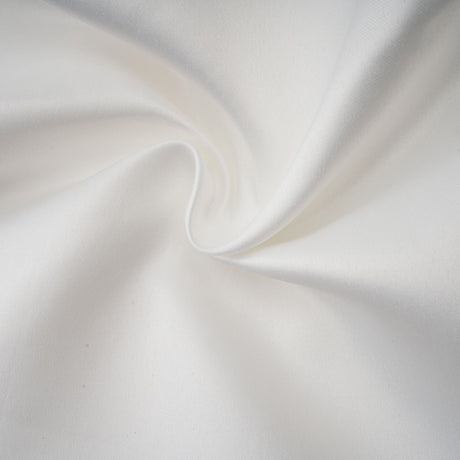 A woman wearing a white halterneck mini dress with ruffles standing against a plain background
